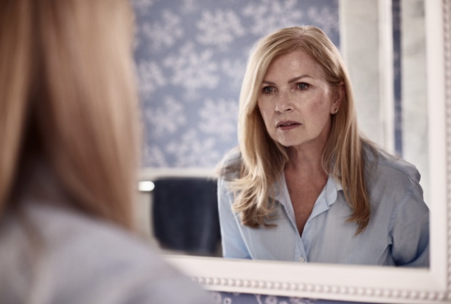 A menopausal woman looks in the mirror with a confused expression.