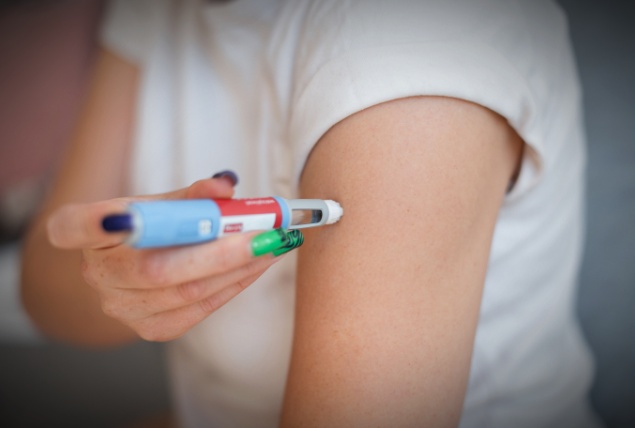 A woman pushes an Ozempic shot into her arm.