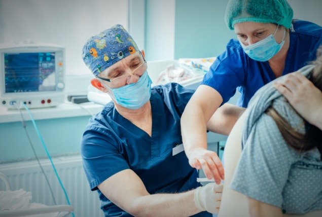 A doctor and a nurse administer an epidural to a pregnant woman during childbirth.