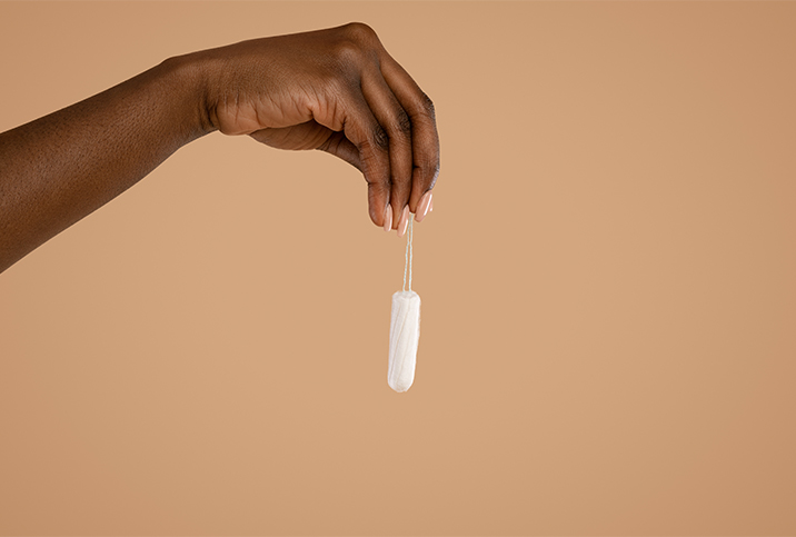 The hand of a black woman is holding a tampon up by the string.