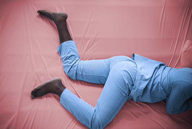 A person in a set of light blue pajamas lays against a pink sheet.