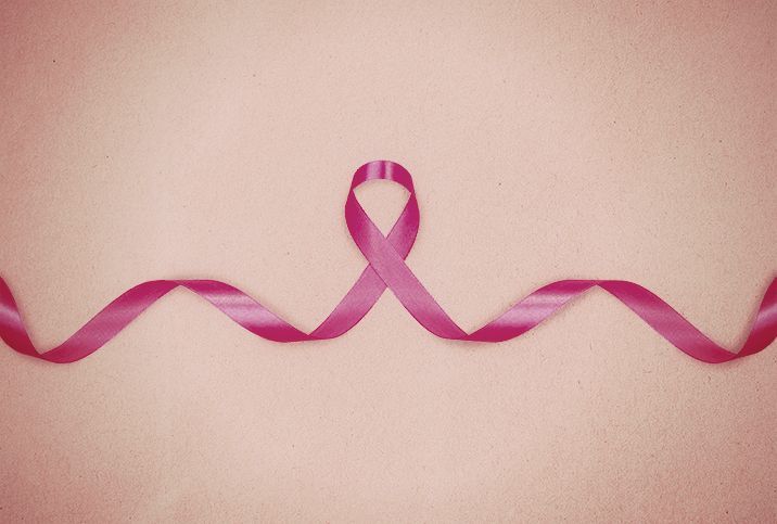 A pink ribbon for breast cancer awareness lays across the light pink surface.