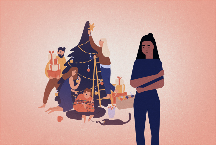 A woman stands away from her family sitting around a Christmas tree.