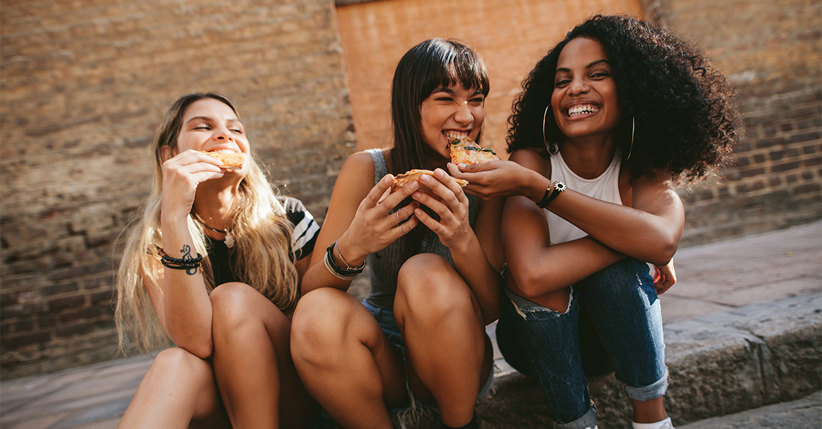 Three women are eating slices of pizza.