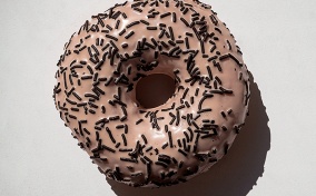 A pink donut with black sprinkles against a white background.