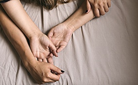 Two people lying together in bed with outstretched arms.