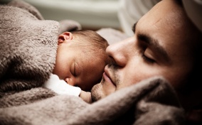 A father holds his newborn baby on his chest while laying down.