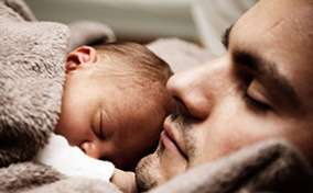 thumbA father holds his newborn baby on his chest while laying down.