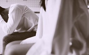 A couple sits on the side of a mattress in distress about erectile dysfunction.