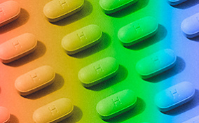 Pills are arranged in a pattern with a rainbow-colored overlay.