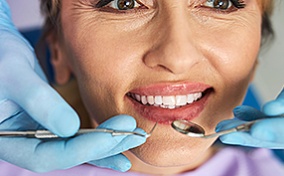 A woman receiving a dental exam from a dentist wearing blue gloves.