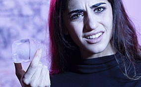 A woman with a confused look holding an ice cube.