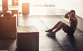 ThumbA man is doing sit-ups in the gym with sunlight shining through the window.