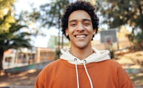 A-teenage-boy-stands-outside-and-smiles-at-the-camera