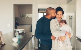 Man-kisses-a-woman-holding-a-baby-in-the-kitchen