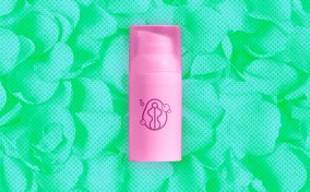 pink-skincare-bottle-sits-against-green-pile-of-petals