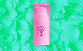 pink-skincare-bottle-sits-against-green-pile-of-petals