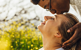 A man leans over a woman and kisses her forehead.