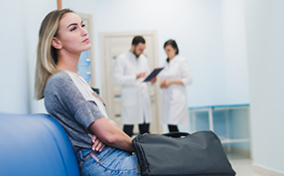 A woman sits on a hospital bench with two doctors in the background.