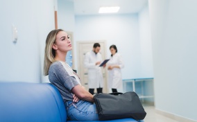 A woman sits on a hospital bench with two doctors in the background.