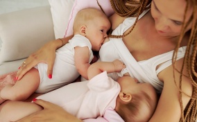 A woman with braids breastfeeds two babies. 