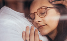 A woman in glasses rest her cheek against her spouse's chest.