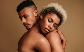 A naked couple embraces with their eyes closed. 