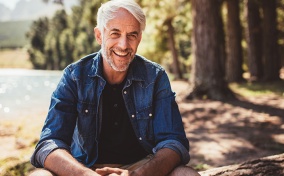 A-white-haired-man-sits-in-the-wood-smiling-at-the-camera