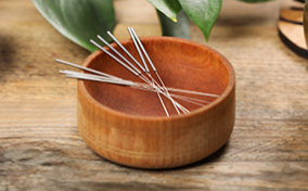 A wooden bowl is holding acupuncture needles.