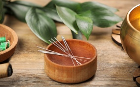 A wooden bowl is holding acupuncture needles.