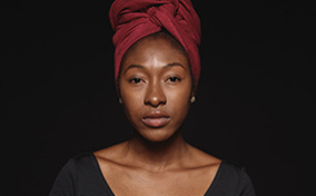 A black woman wearing a head wrap looks at the camera.