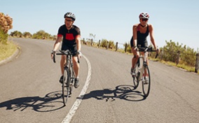 Two men ride their bikes toward the camera with the sky behind them. 