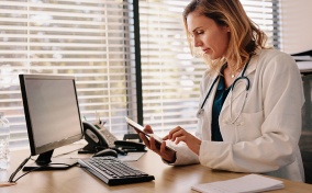 A doctor sits at a desk and looks at a tablet. 