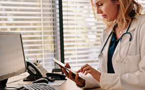 A doctor sits at a desk and looks at a tablet. 