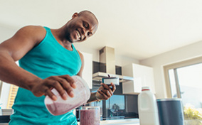 A smiling man pours himself a purple smoothie.