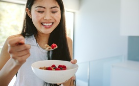 A smiling woman eats granola and berries. 