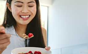 A smiling woman eats granola and berries. 