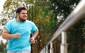 A man runs down the street, wearing blue and listening to music.