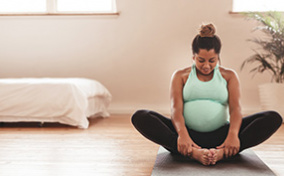 A smiling pregnant person sits ion a yoga mat in butterfly pose.