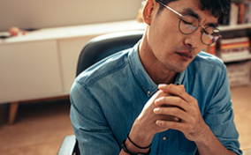 A man in glasses leans his head to the side with closed eyes and a distressed expression.