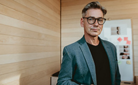 A man stands with his cellphone in hand looking at the camera.