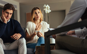 A man rubs his face while his partner talks to a licensed professional during couples therapy.