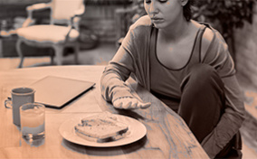 A woman stares tentatively at a plate of food blocked partially by her hand.