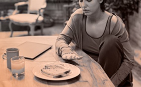 A woman stares tentatively at a plate of food blocked partially by her hand.