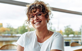 A woman sitting in a cafe smiles at the camera.