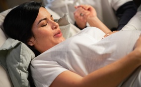 A woman in labor breathes with her eyes closed while holding hands with another person.