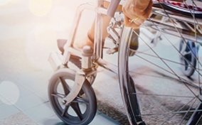 A person sits in a wheelchair and holds the frame with the sun shining down on them.