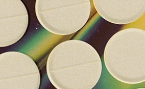 Multiple white opioid pills repeat over a holographic background.