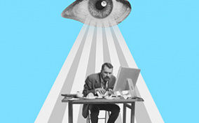 An eye beams down on a stressed man working at his desk.