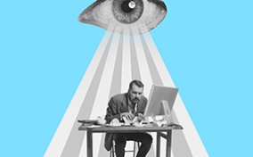 An eye beams down on a stressed man working at his desk.